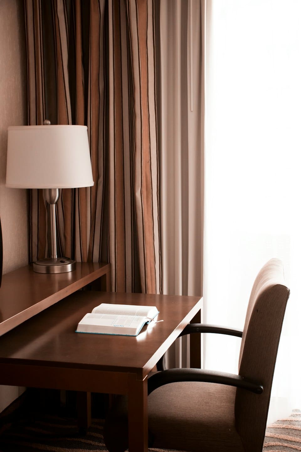 An open book sits on a wooden desk near a lamp.